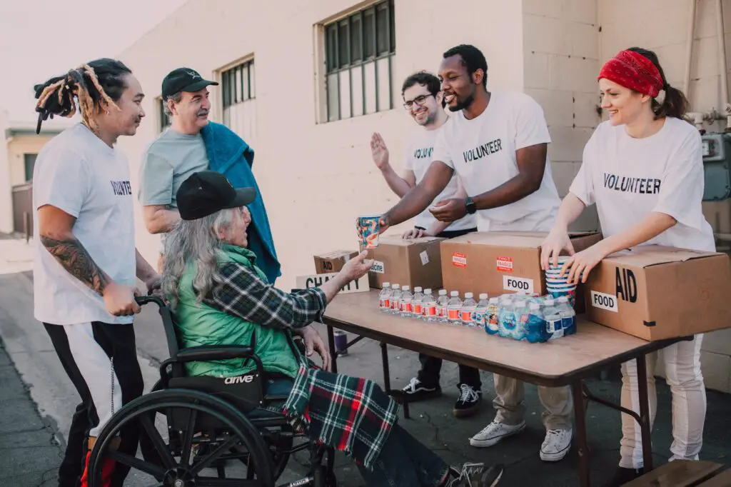 a group of volunteers assisting an elderly person on a black wheelchair for charity